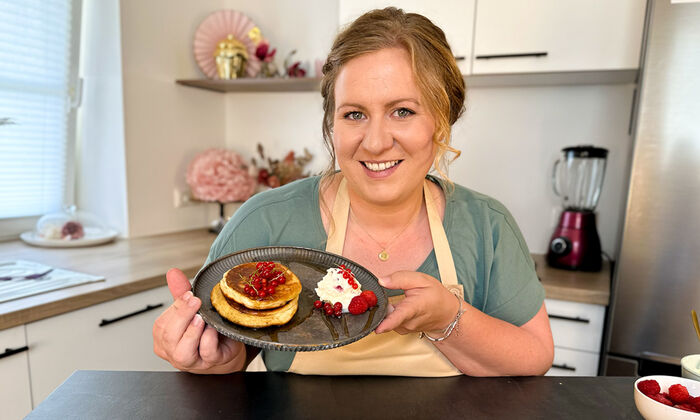 Rezepte & Inspirationen: Monika Nagl zeigt lächelnd ihre japanischen Pfannkuchen mit Mascarpone und Butter auf einem grauen Teller.