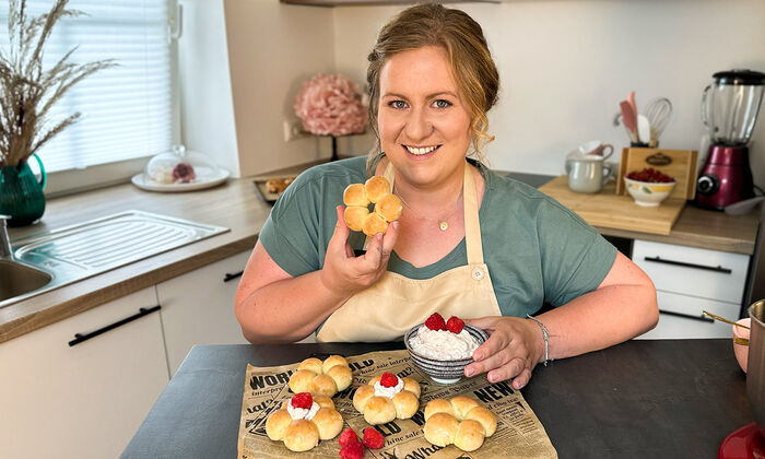 Rezepte & Inspirationen: Monika Nagl zeigt lächelnd ihre Mochi-Donuts mit Mascarpone und Butter auf einem braunen Zeitungspapier.