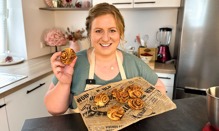 Rezepte & Inspirationen: Monika Nagl zeigt lächelnd ihr Franzbrötchen Rezept Original mit Butter auf einem braunen Zeitungspapier.